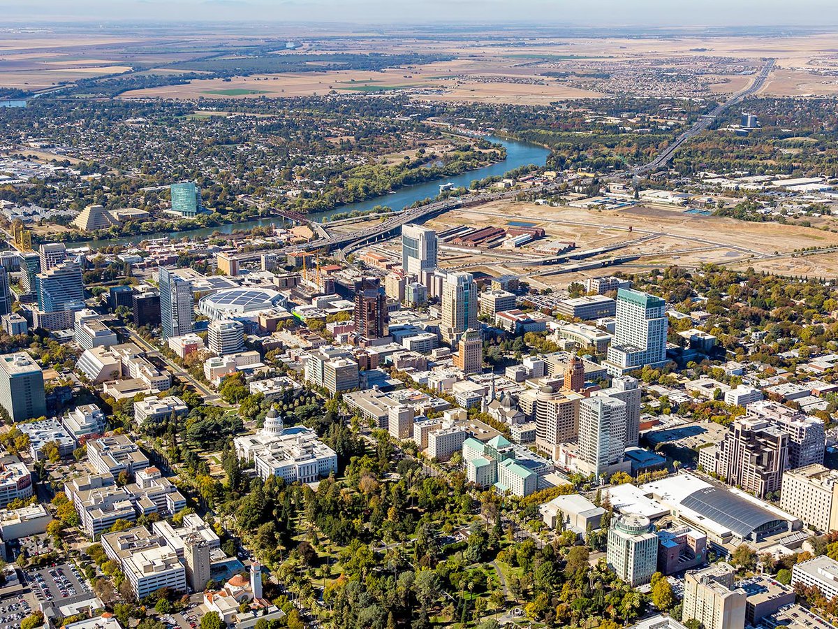 Aerial photo of Downtown Sacramento, with the iconic State Capitol Building as the centerpiece, surrounded by an array of high-rise buildings and the Sacramento River flowing in the background.