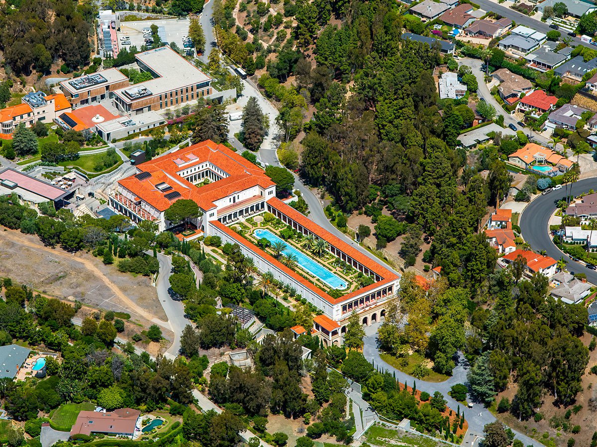 A close-up aerial view of the Getty Villa reveals its stunning Roman-inspired architecture, complete with vibrant ceramic rooftops and a majestic pool that epitomizes the grandeur of ancient luxury.