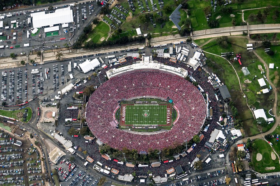 Aerial view of the Rose Bowl Stadium during the 2026 game, showing a full stadium with Indiana and Alabama logos in the endzones. A dark gray B-2 Spirit stealth bomber is captured in flight directly over the northern parking lot and Brookside Golf Club.