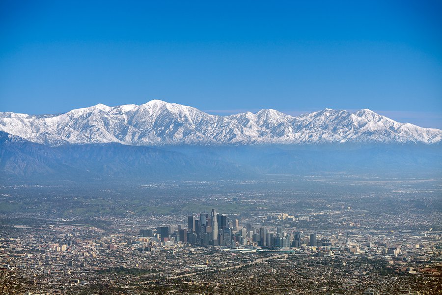 An aerial photo showing a breathtaking view of snow-capped mountains towering over the bustling metropolis of Downtown Los Angeles, marking a rare phenomenon during California's wet and cold winter season.