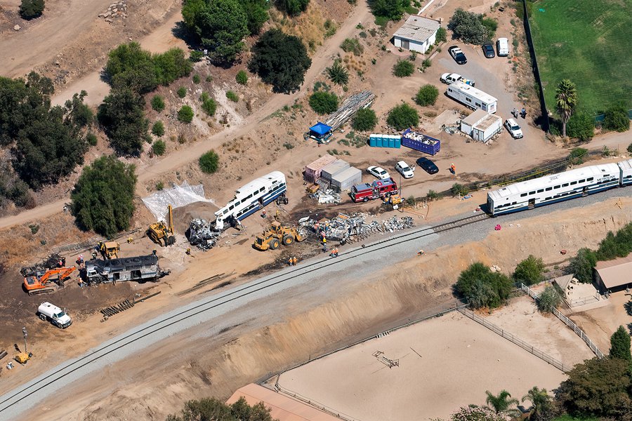 Close-up oblique aerial image of the 2008 Chatsworth train collision, highlighting the damaged train cars, various emergency vehicles, and personnel working on the ground near an equestrian facility.