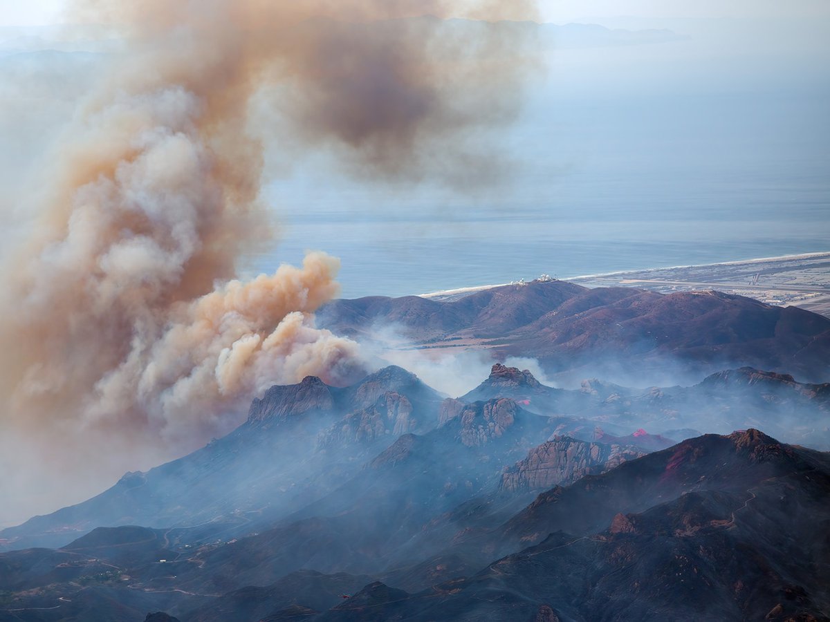 Aerial view of the Santa Monica Mountains during the Woolsey Fire in November 2018, showing smoke billowing over the Pacific Ocean, Point Mugu NAS, and surrounding landscape.