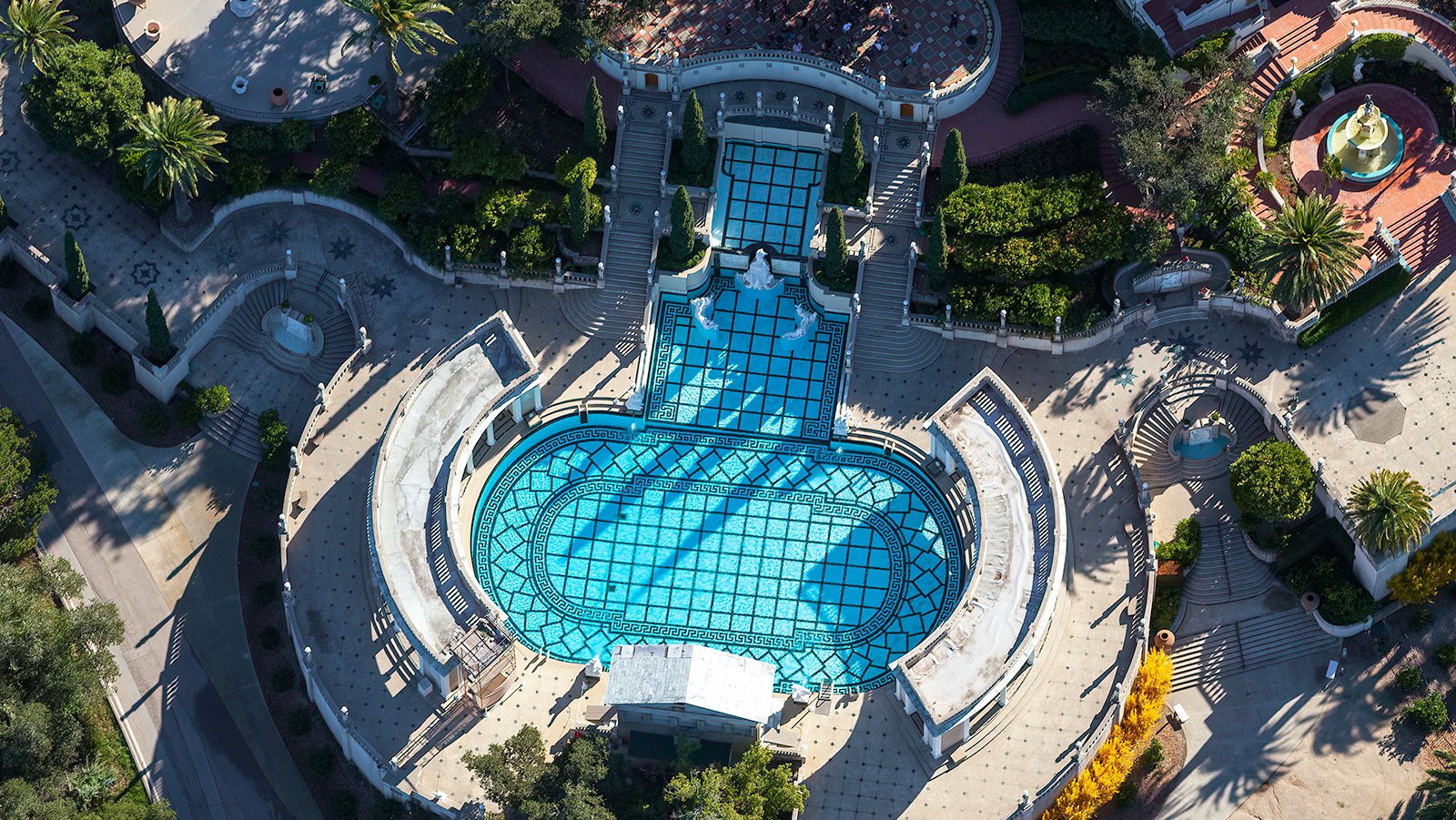 An aerial photograph of the iconic Hearst Castle Neptune Pool showcases its grandeur, with its deep blue waters surrounded by intricately designed marble columns and sculptures