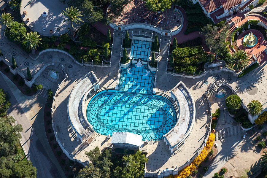 An aerial photograph of the iconic Hearst Castle Neptune Pool showcases its grandeur, with its deep blue waters surrounded by intricately designed marble columns and sculptures