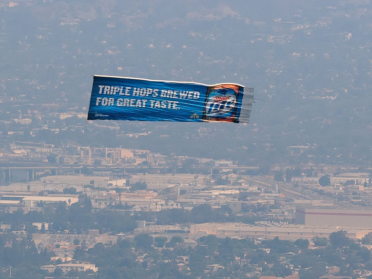 Air-to-air photograph of a Miller Lite banner being towed over santa Monica Beach on a busy day