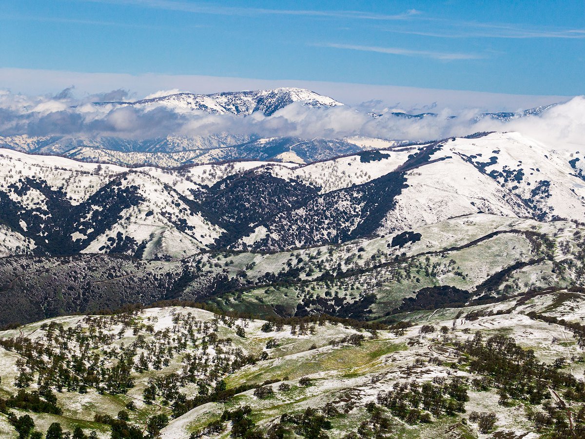 Blog photo of snowy mountains with green vegetation just peaking through, showing the springtime is here